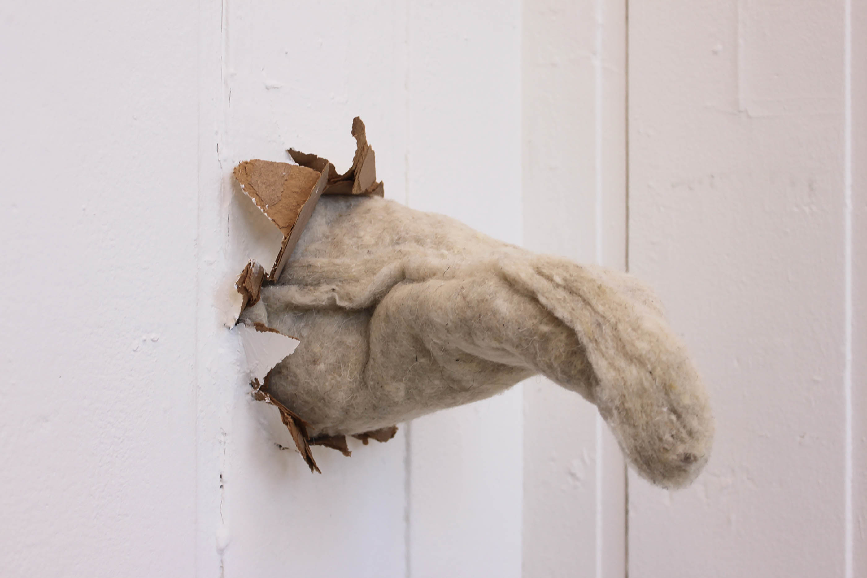 A small sculpture made of wool insulation bursts through the wall
