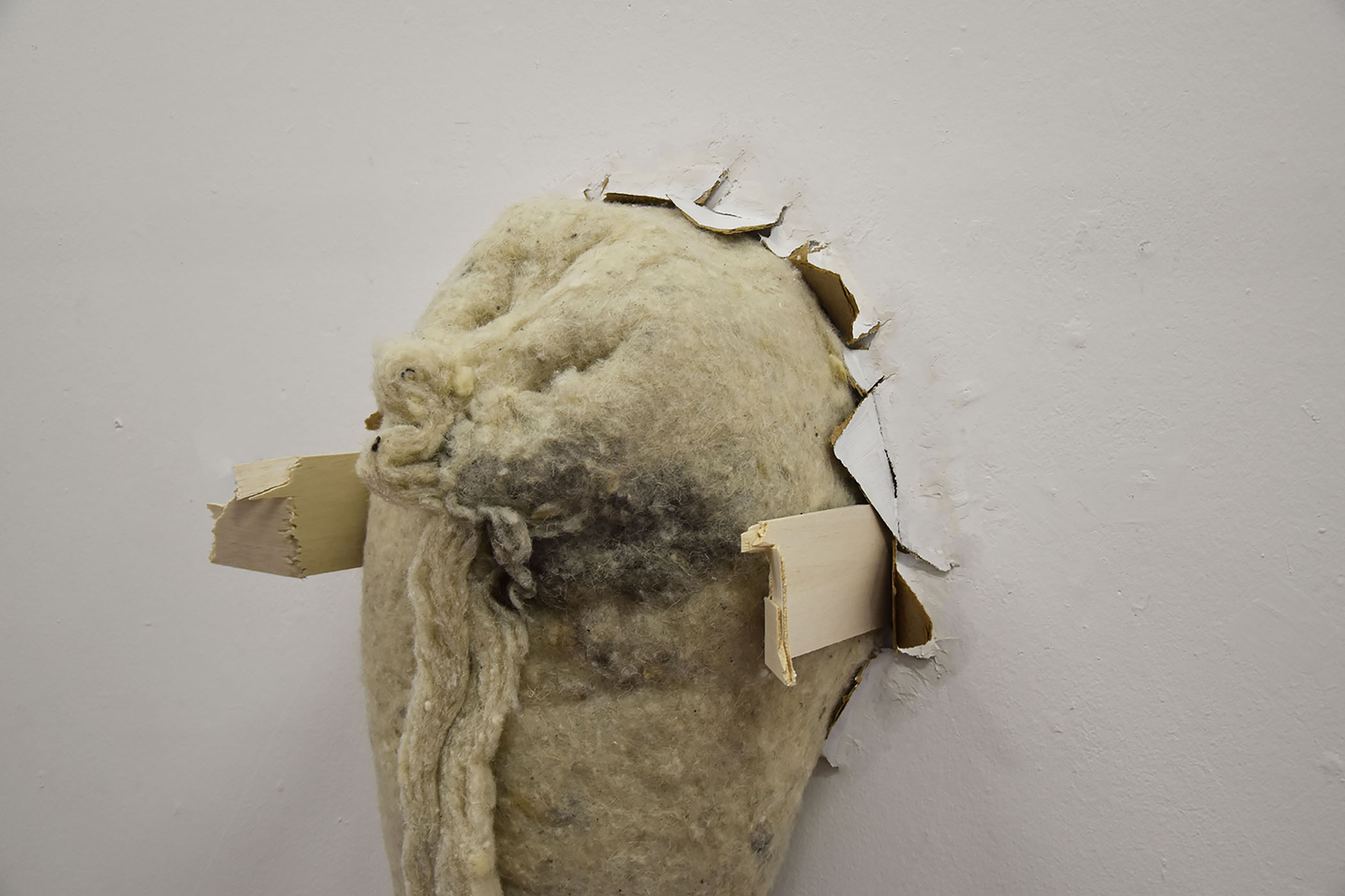 Close-up of a sculpture made from wool insulation and wood bursting from the wall.
