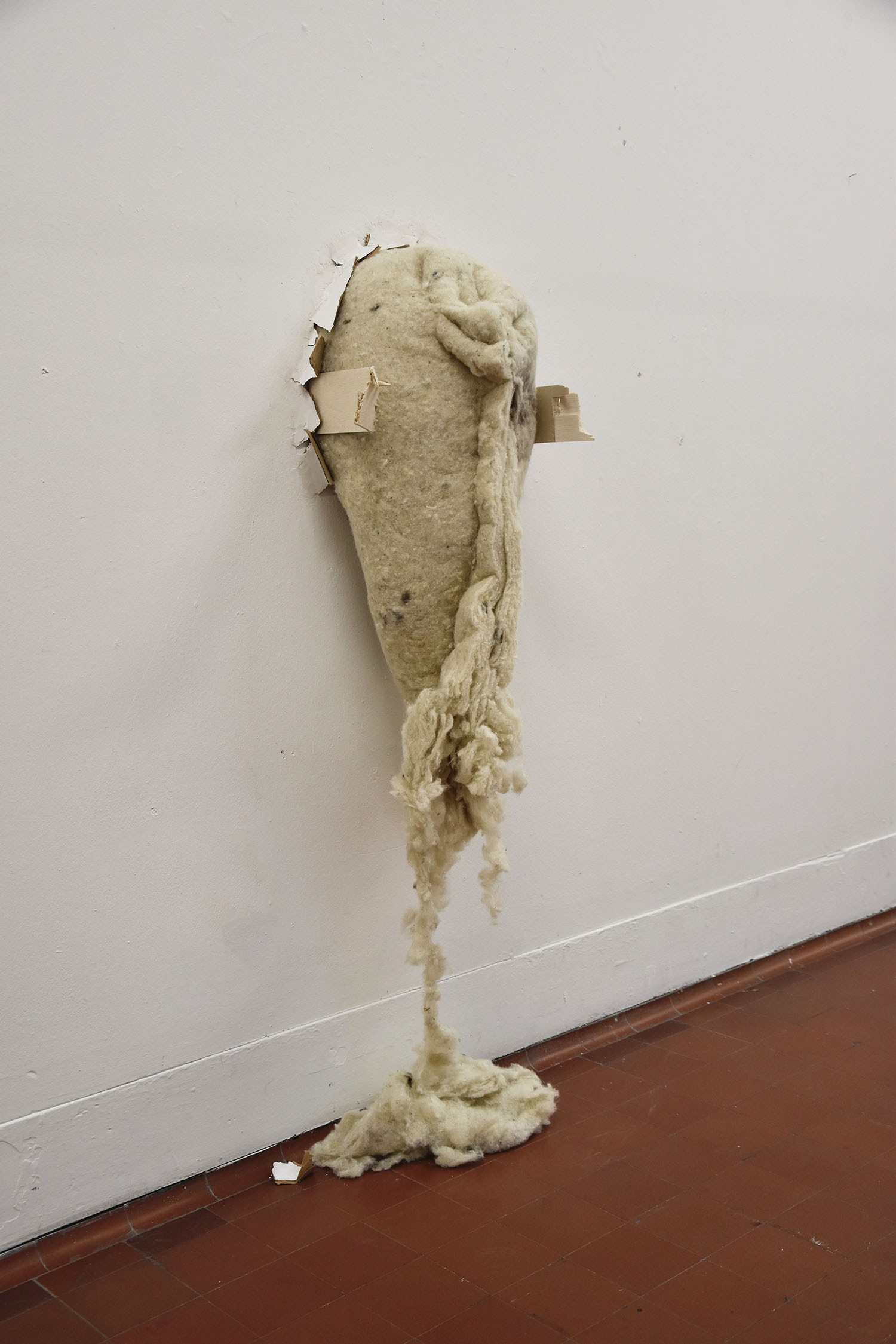 Sculpture made from wool insulation and wood bursting from the wall