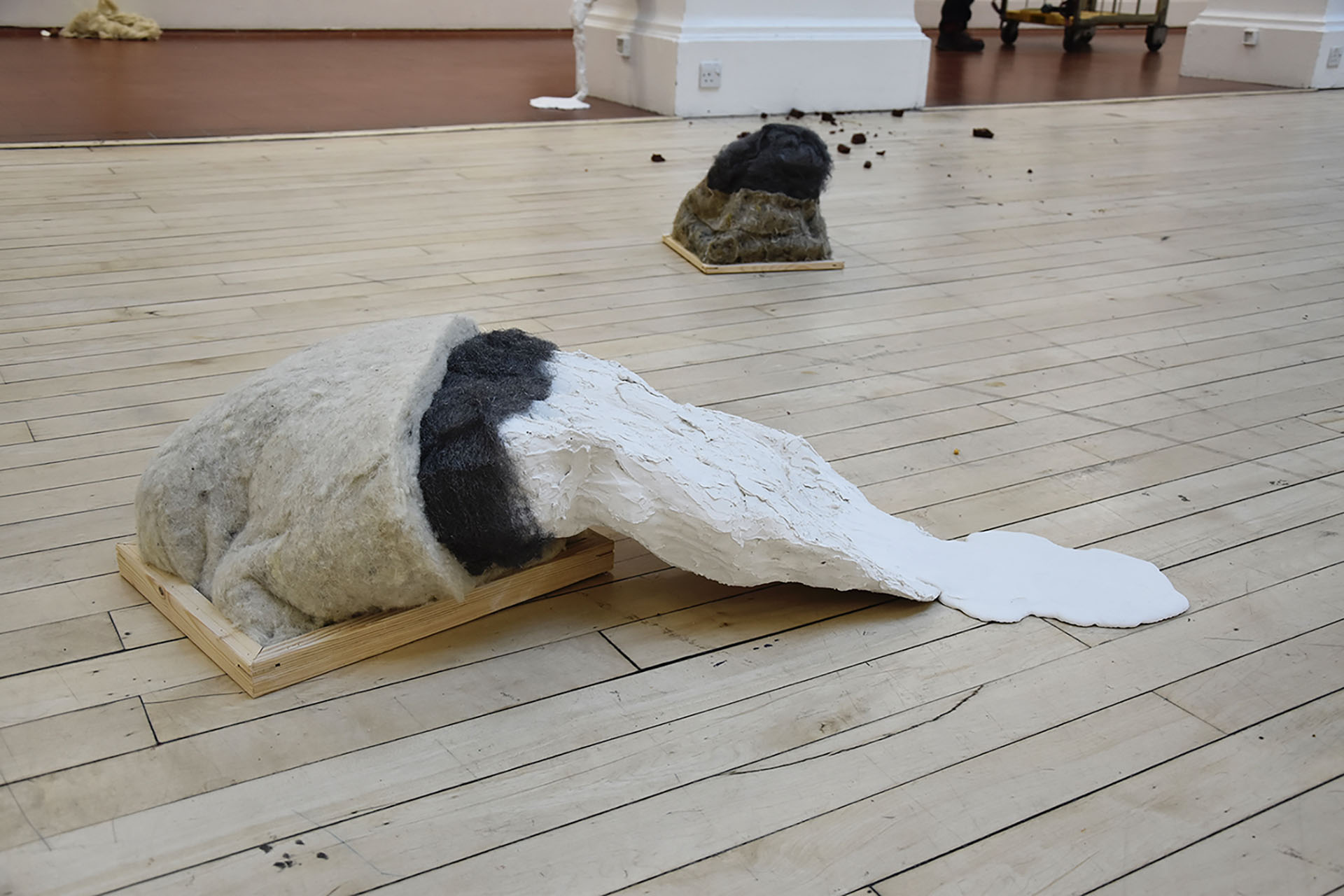 Sculpture made from wool insulation, steel wool, and puddling Polyfilla emerges from a wooden frame on a wooden floor