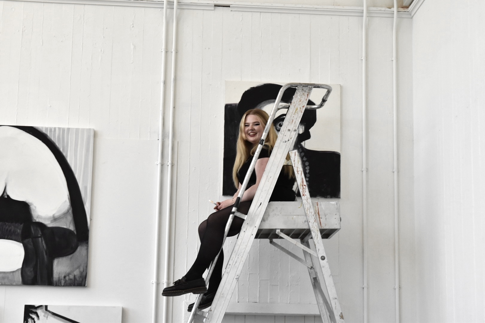 the artist sitting at the top of a tall ladder while installing her degree show work