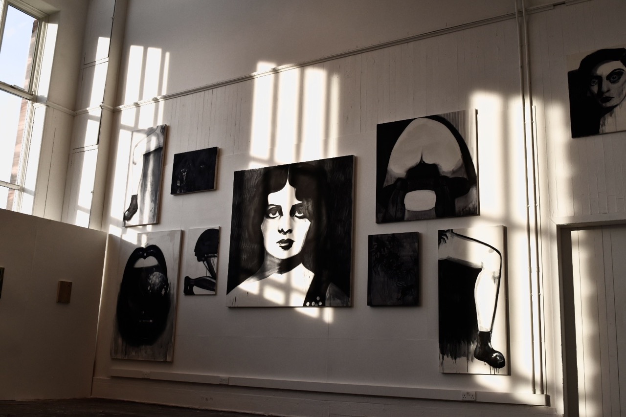 large wall collage of black and white canvases with evening sunlight cast on it through the windows 