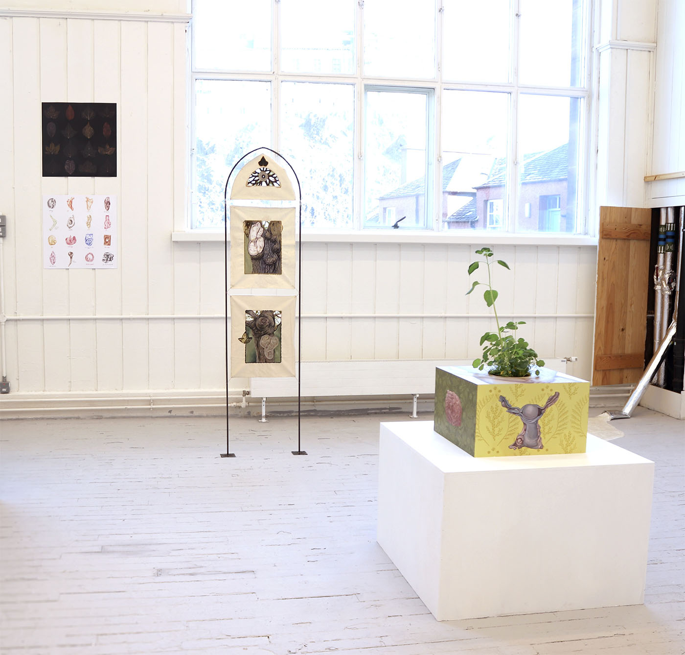 Anna's Degree Show installation with a box-like painting, a metal stand, and two prints on a wall.