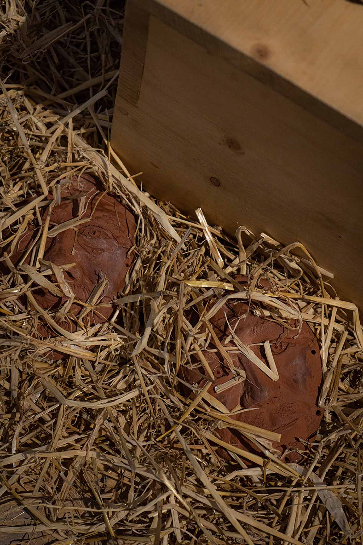 two ceramic faces hidden beneath straw.
