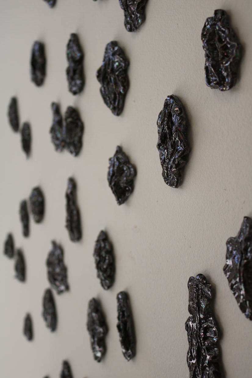 Terracotta vulvas on a wall made in dark opal lustre.