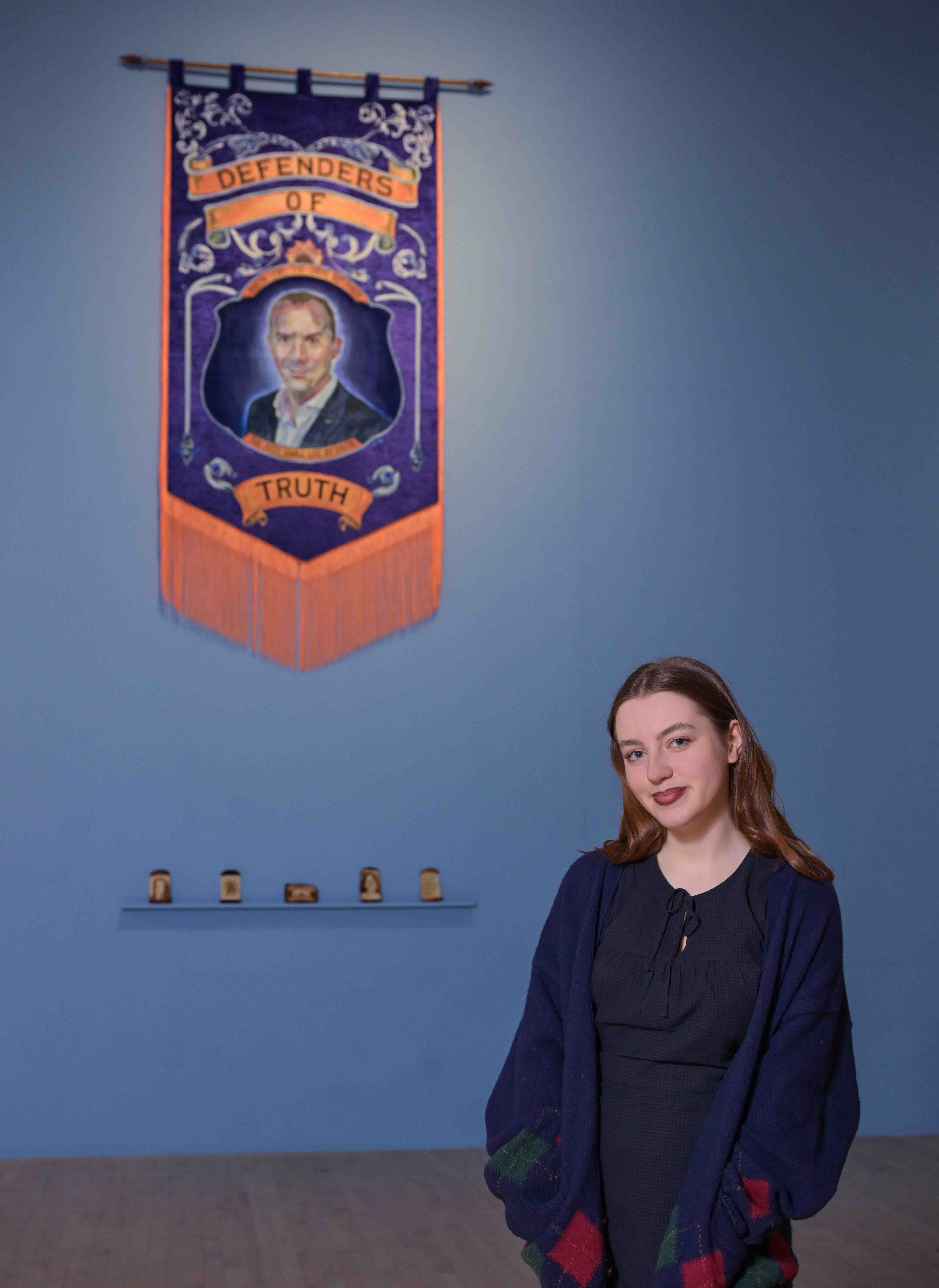 Artist Eilidh McKeown stood in front of orange and purple banner.