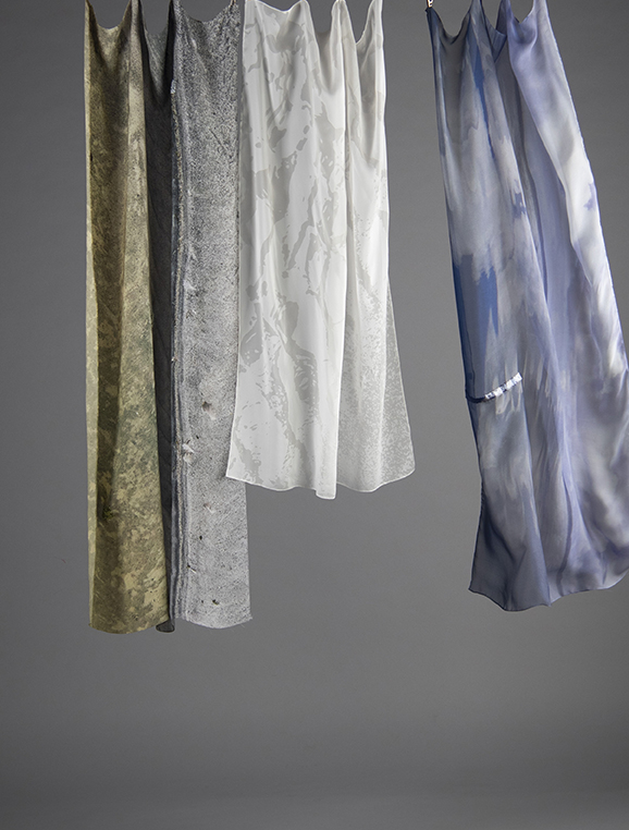 Three silk samples blowing in a slight breeze against a grey background. Each sample has been digitally printed with landscape photography from the Isle of North Uist, and has a small section of beading applied to it, designed to catch the light.