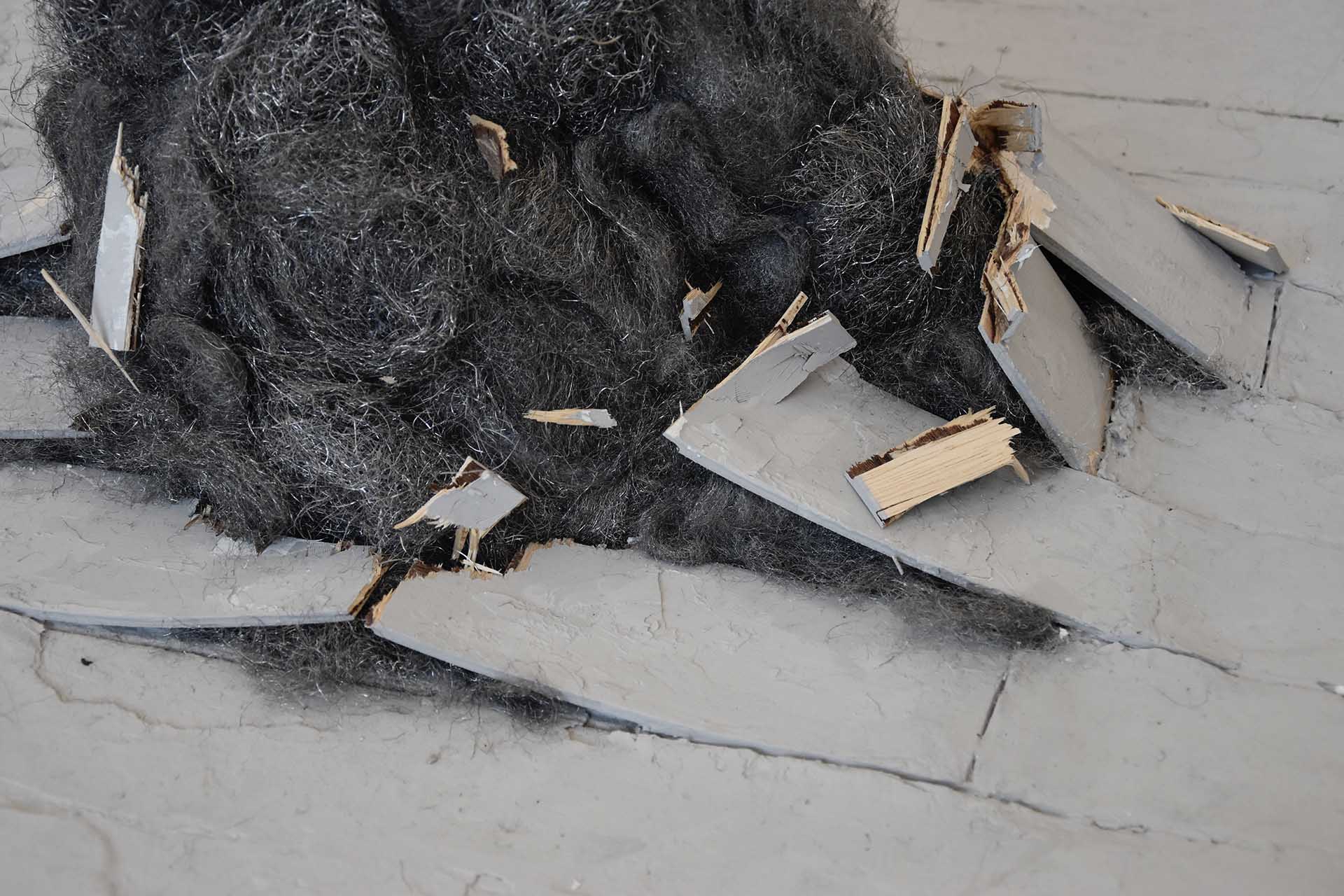 Close up image of a steel wool sculpture emerging from the floorboards.