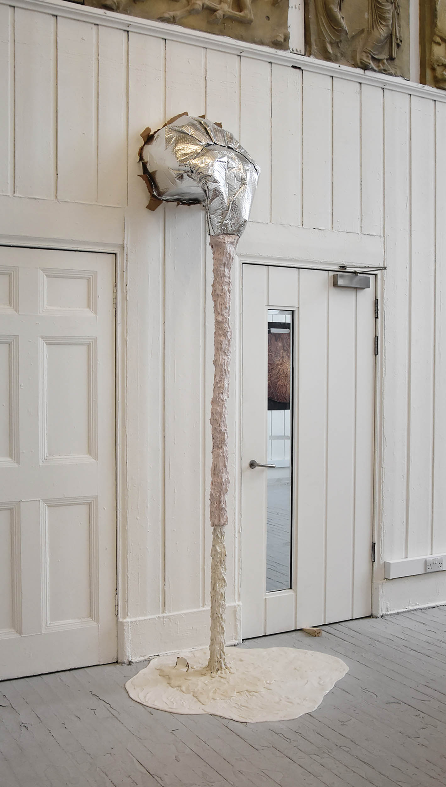 Sculpture made of foil insulation, silicone, and Polyfilla bursts from the wall and spills onto the floor.