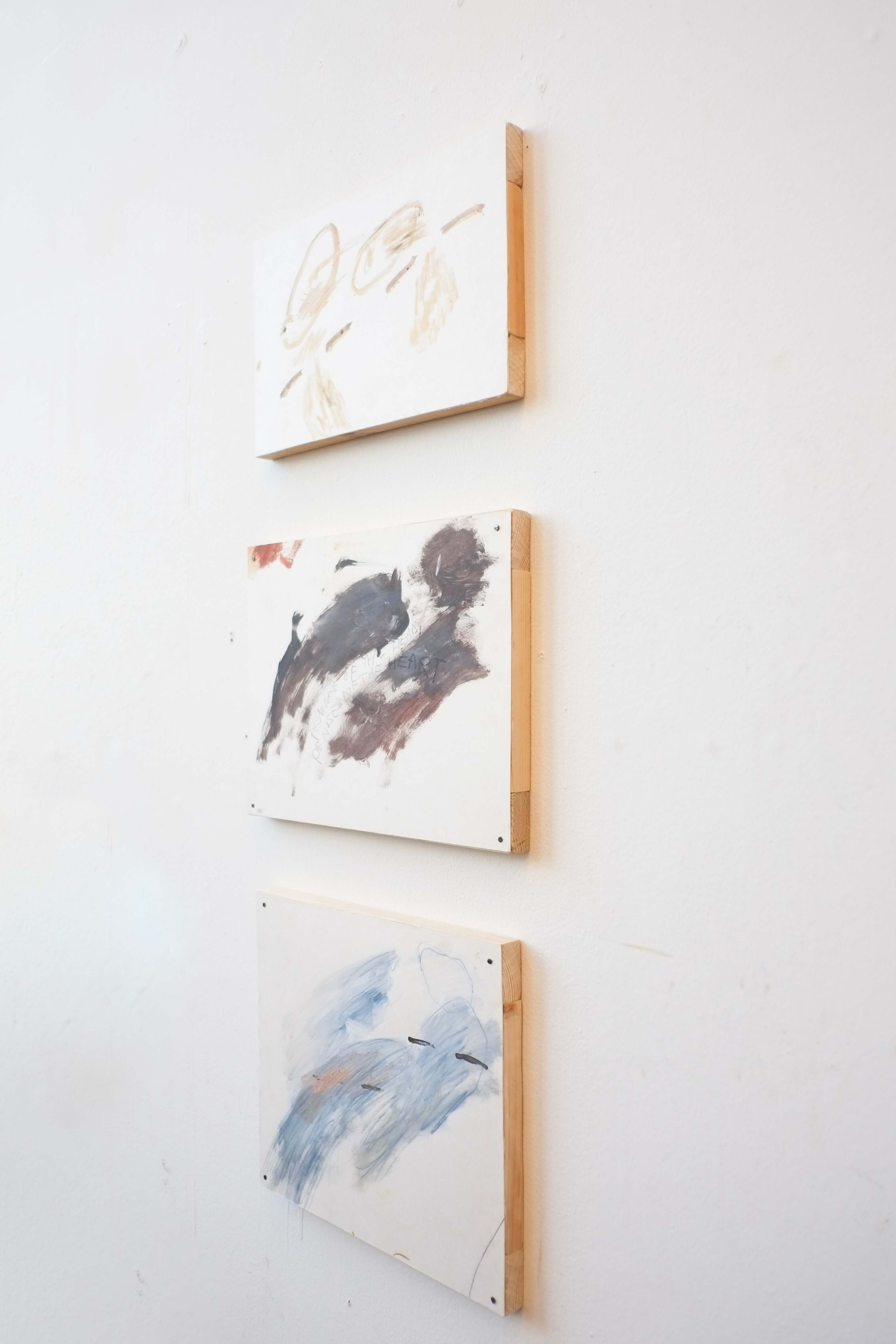 Vertical line of three small paintings/drawings installed on wooden frames