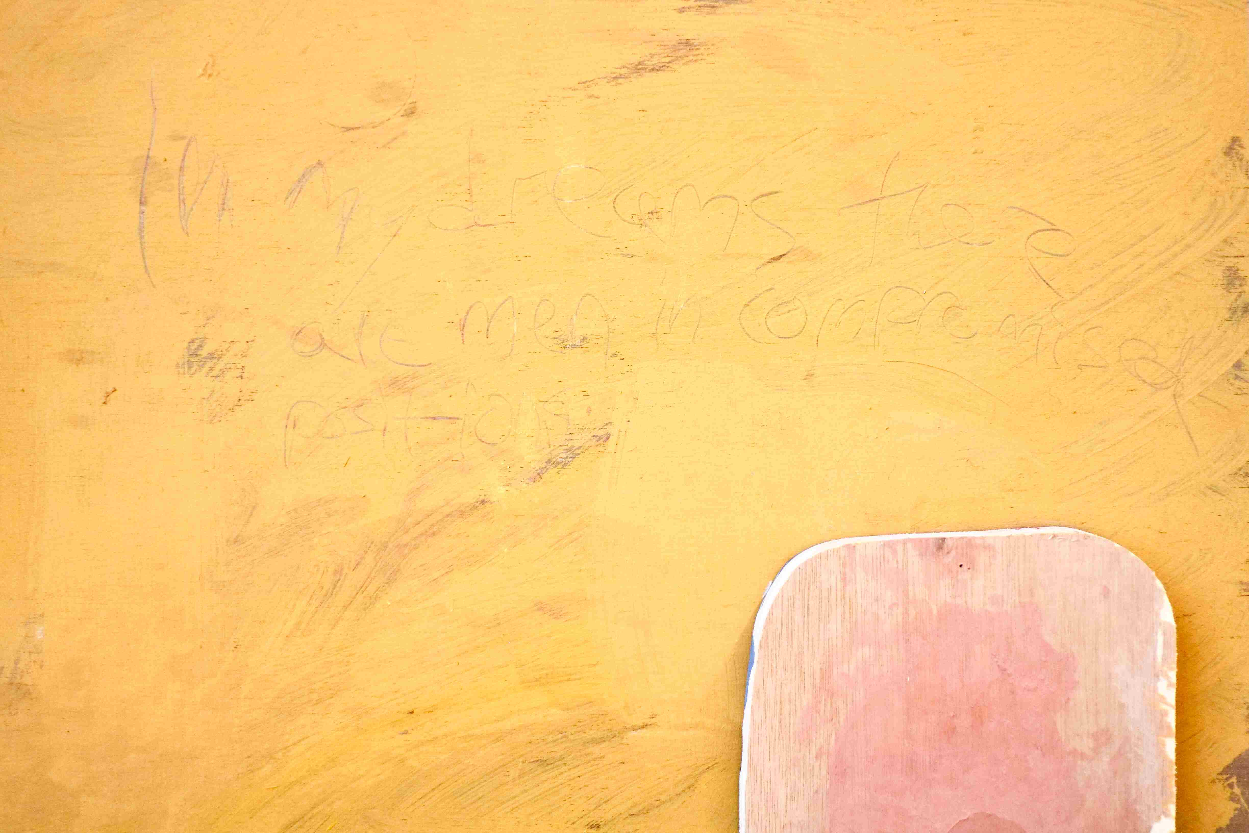 Close up of a vibrant golden-yellow painting on wood. The words 'In My Dreams There Are Men In Compromised Positions' can be seen scratched into the paint