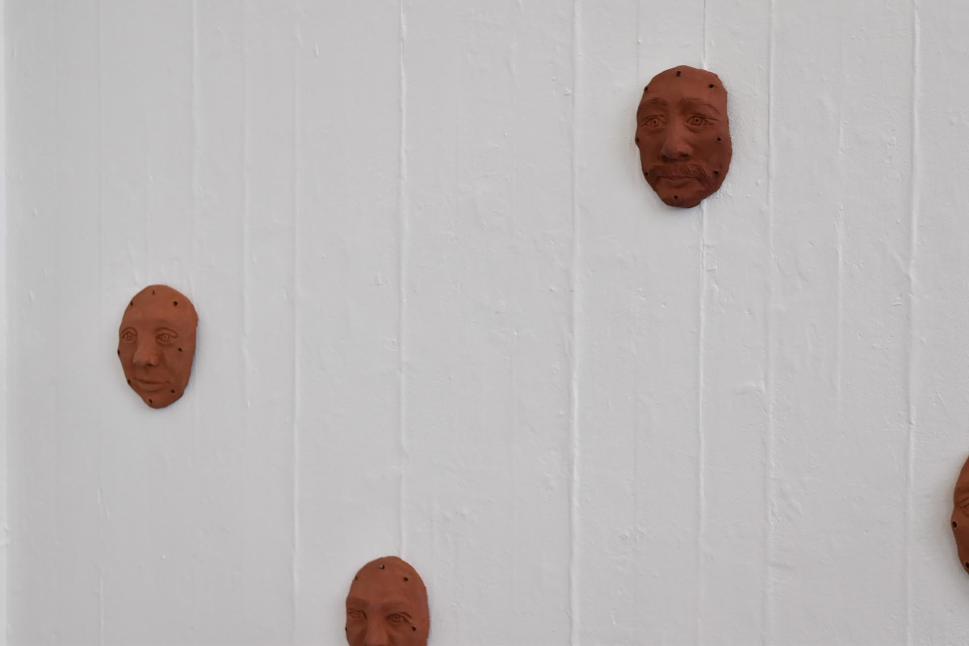 a wall displaying ceramic faces at different heights and levels. 