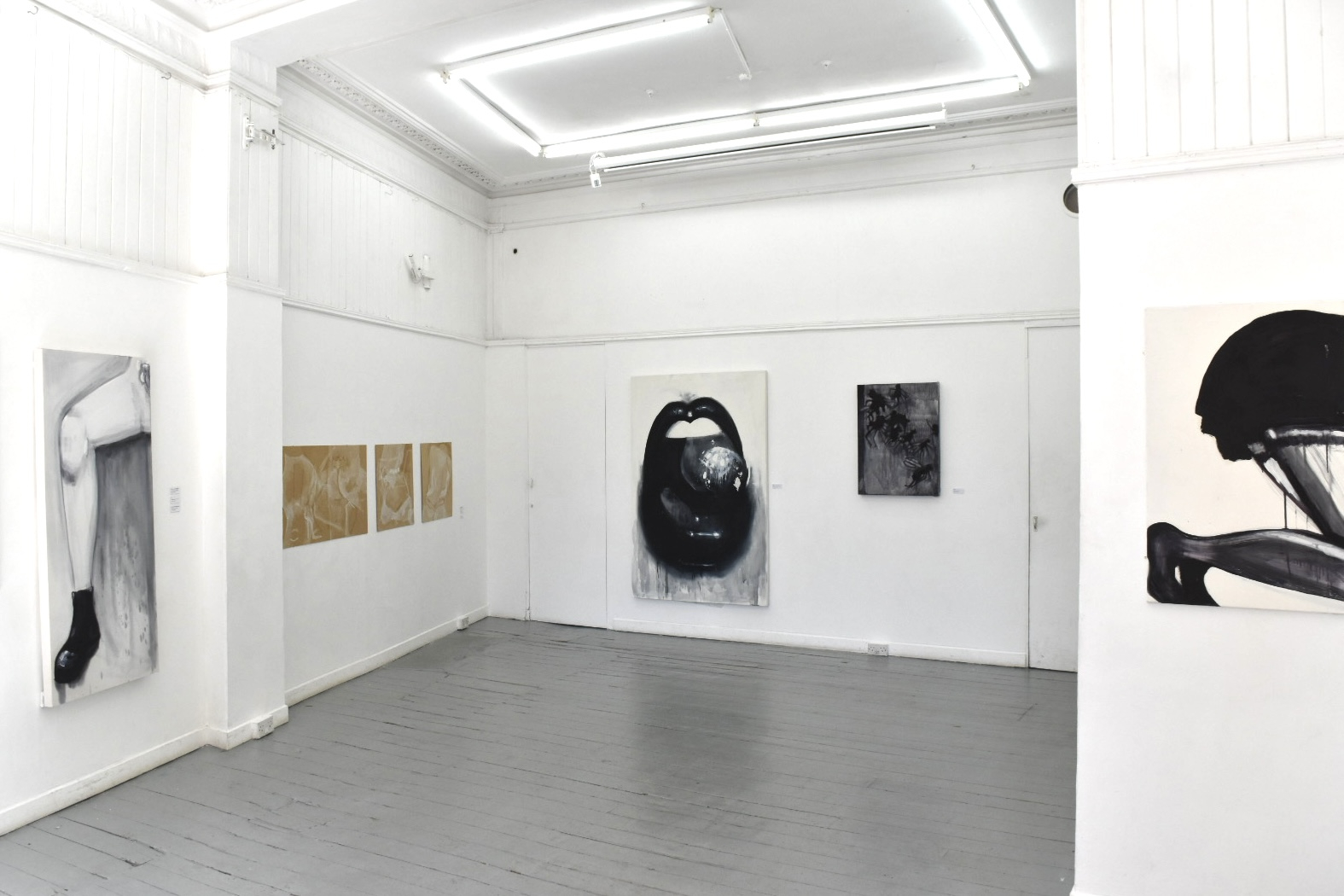 exhbition setting with lots of leg paintings, big mouth and dead flies in black and white, alongsid brown and white paintings