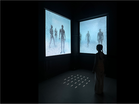 A viewer stands before two large frosted screens showing human silhouettes, with glowing figures on the floor.