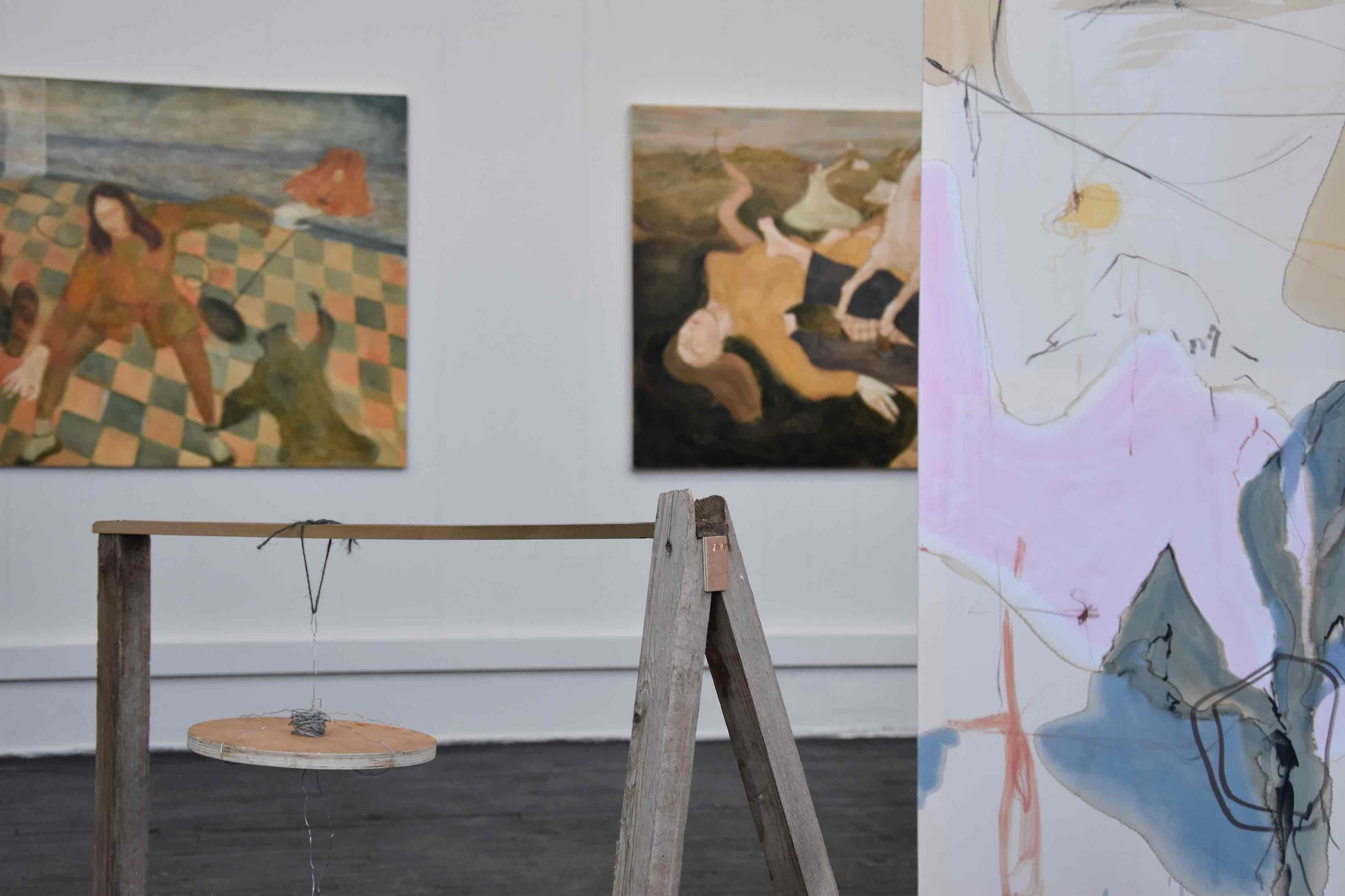 Grad show install, paintings on wall and in foreground next to assemblage 