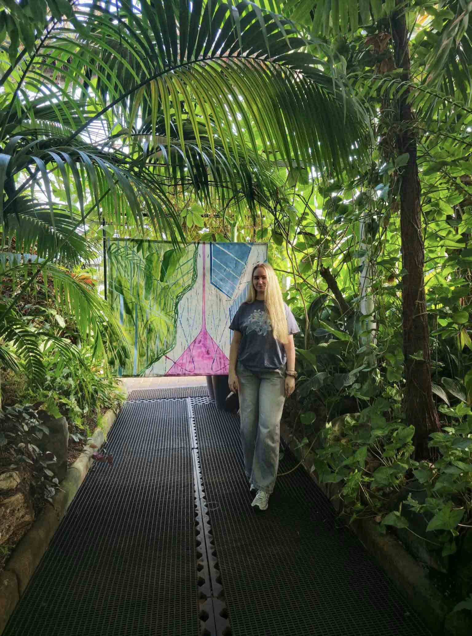 Artist standing in front of her painting installed in the Glasgow Botanic Gardens.