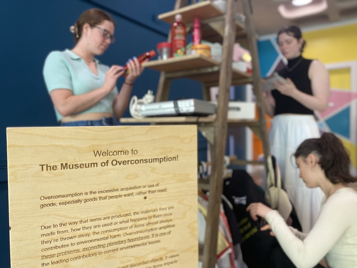 The Museum of Overconsumption sign with people attending the museum in the background