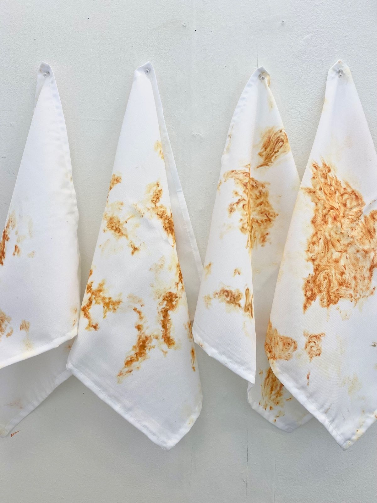 four white cloth napkins hanging on the wall with stains created in paint made to look like food