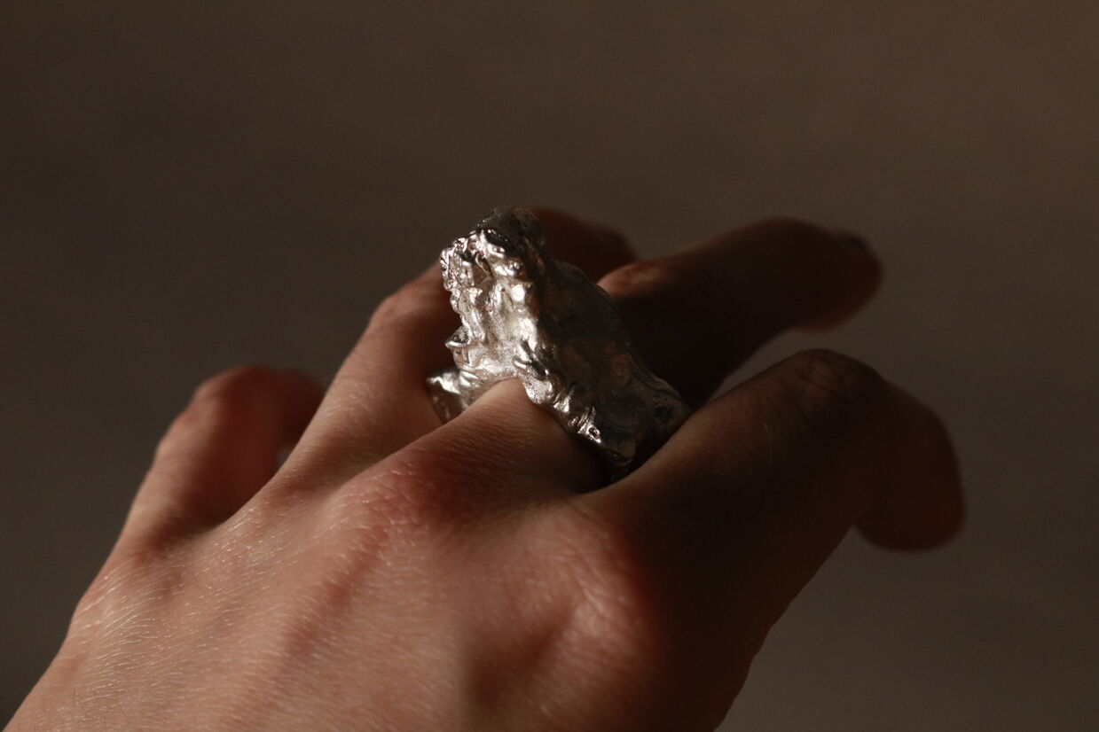 Pewter ring of a vulva being worn.
