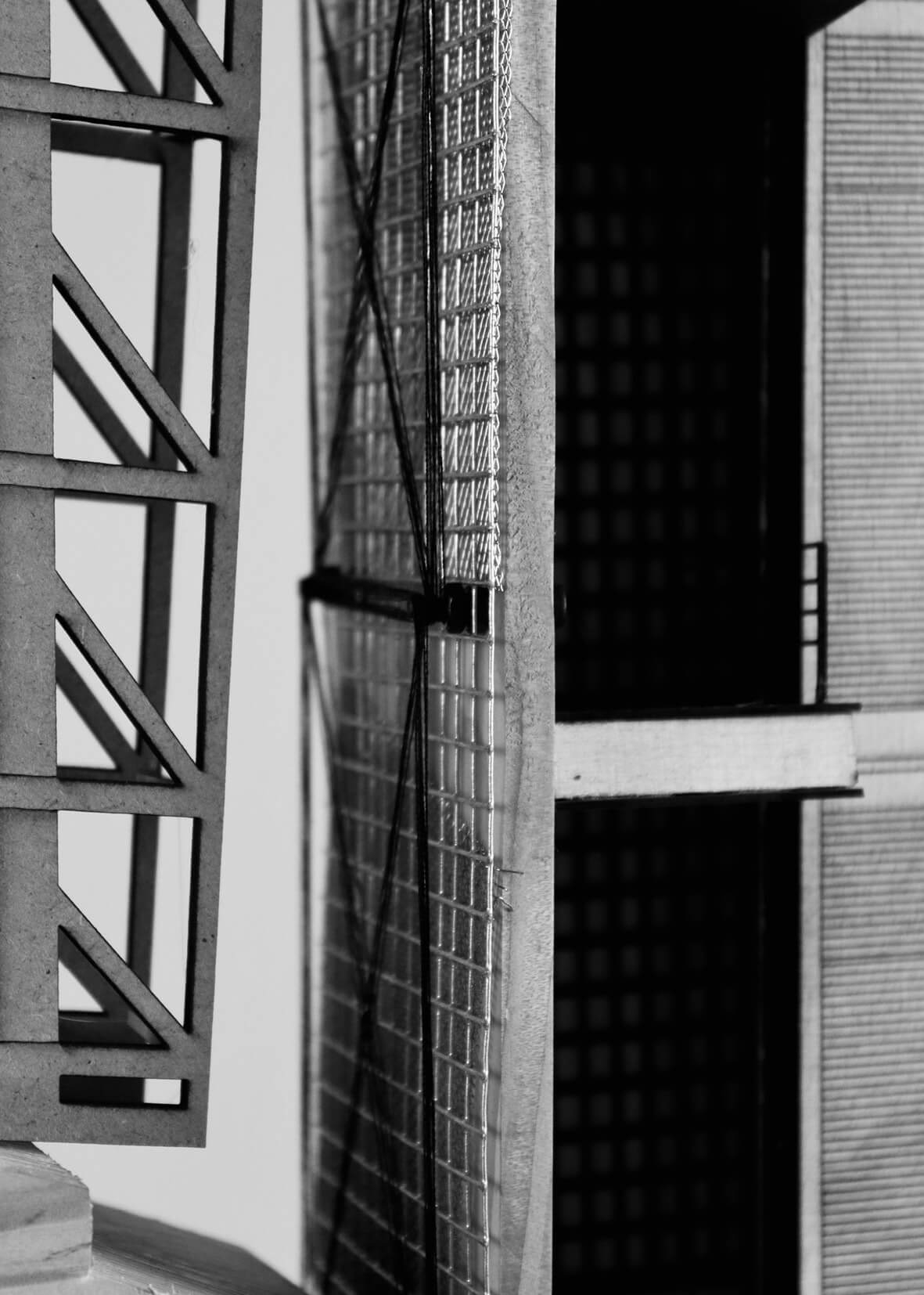 Close-up black and white photograph of a cooling tower 1:50 model showcasing intersecting façade systems. On the left, a laser-cut structural frame contrasts with a central tensioned mesh and grid assembly featuring string or wire bracing. To the right, layered interior and exterior surfaces suggest spatial depth.
