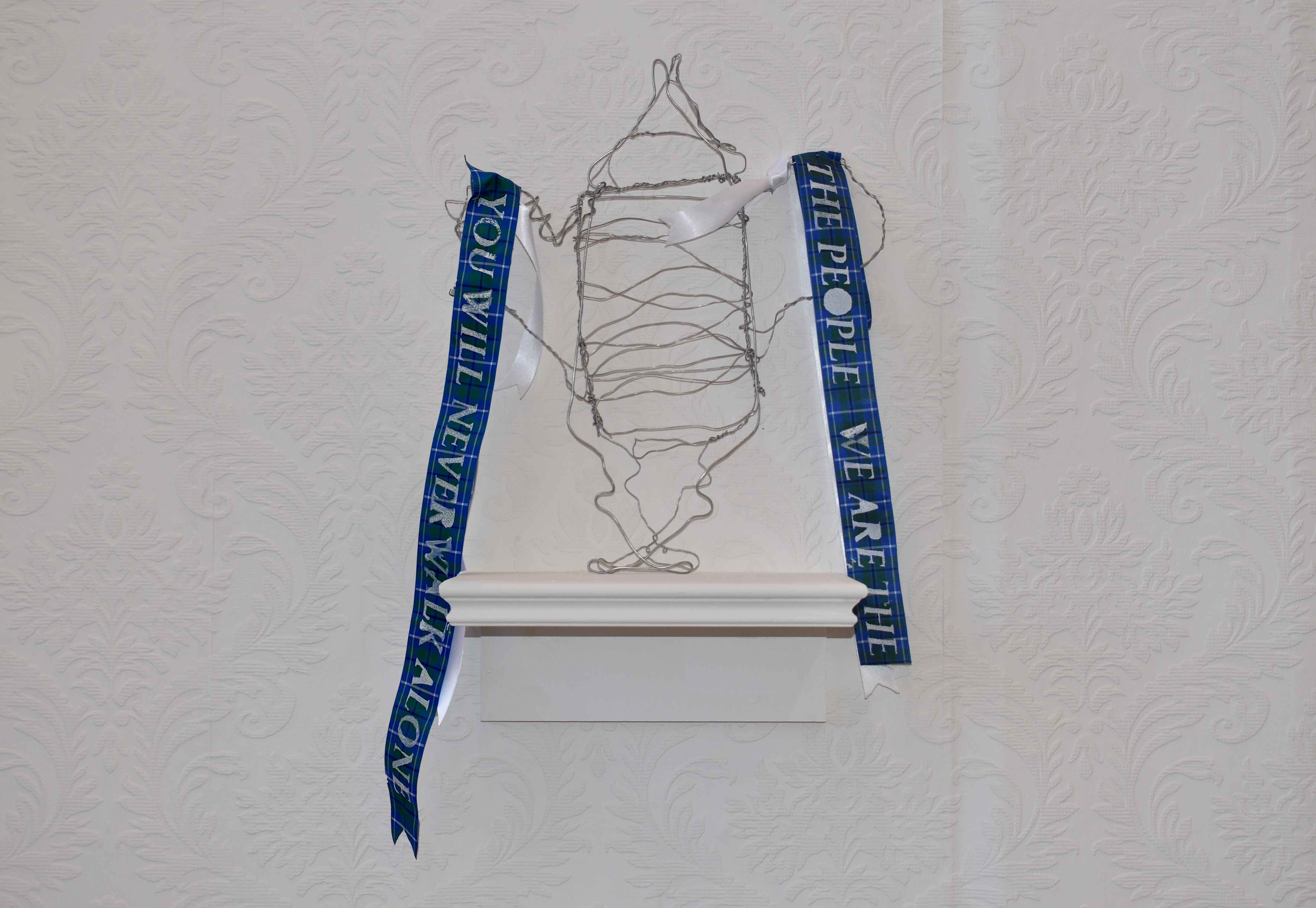 Wire trophy with blue tartan ribbons either side sporting white text reading 'you will never walk alone' and 'we are the people'