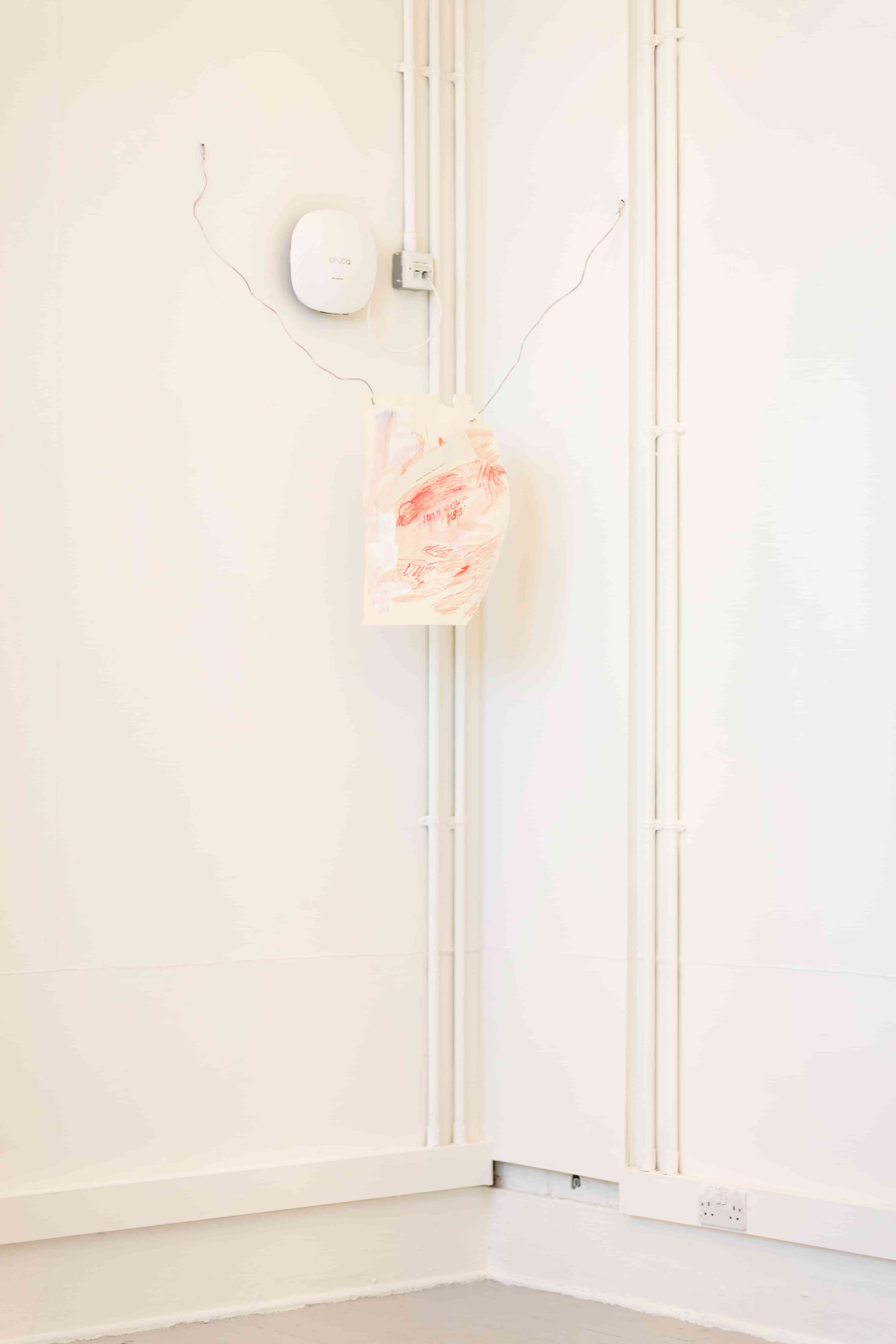A white and red artwork on paper suspended in a corner with two lengths of wire
