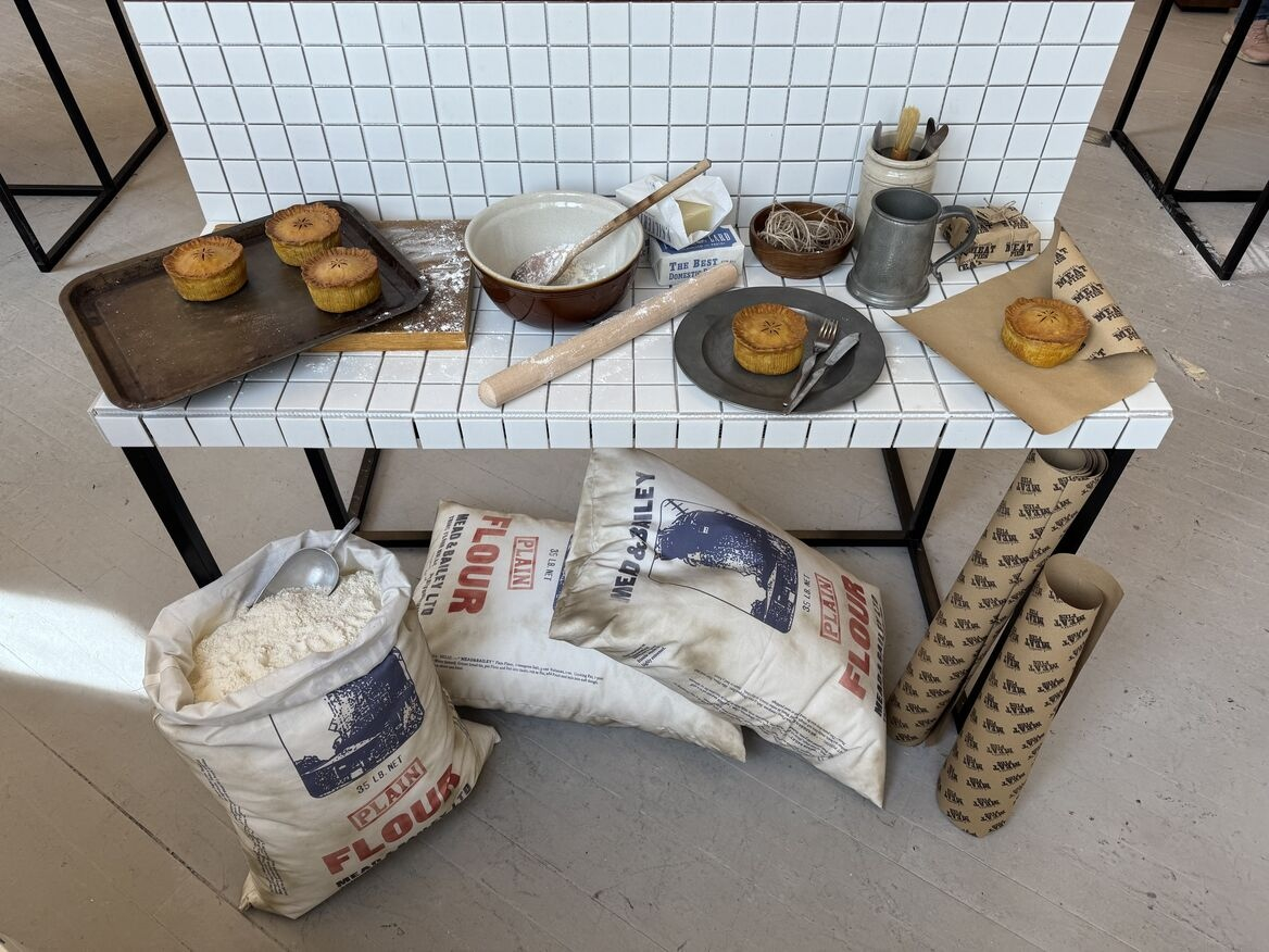 A tiled kitchen display showing graphics props (flour bags, lard and pie packaging) in situ along with pies and various baking utensils 