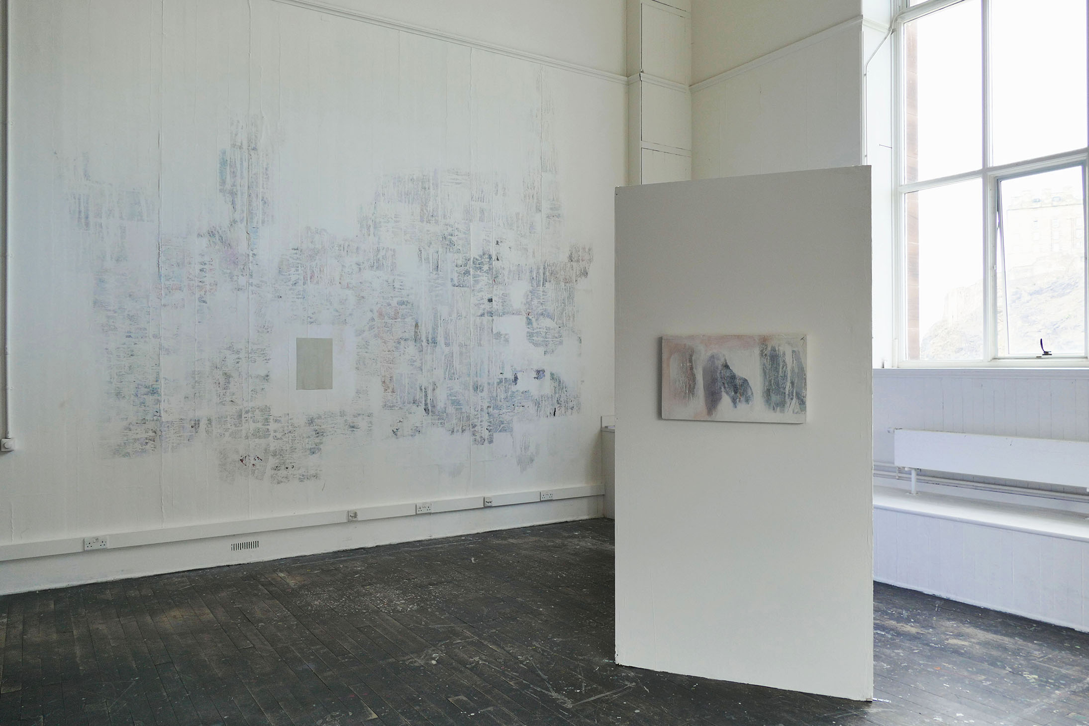 a white L-shaped screen with paintings on it, adjacent to a mural resembling torn down posters 