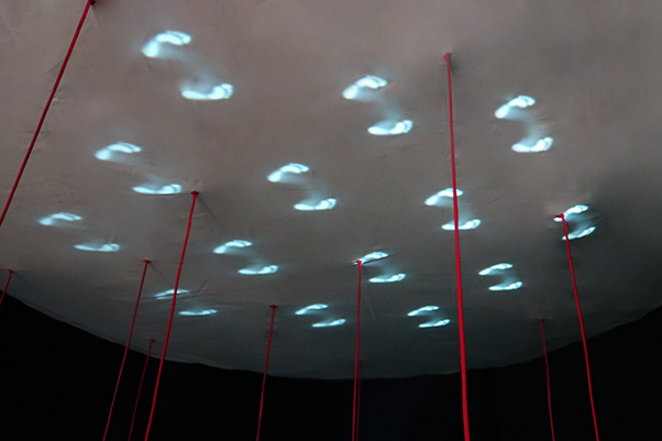 Glowing footprints figures projected on the underside of a white canopy, with red strings hanging down.