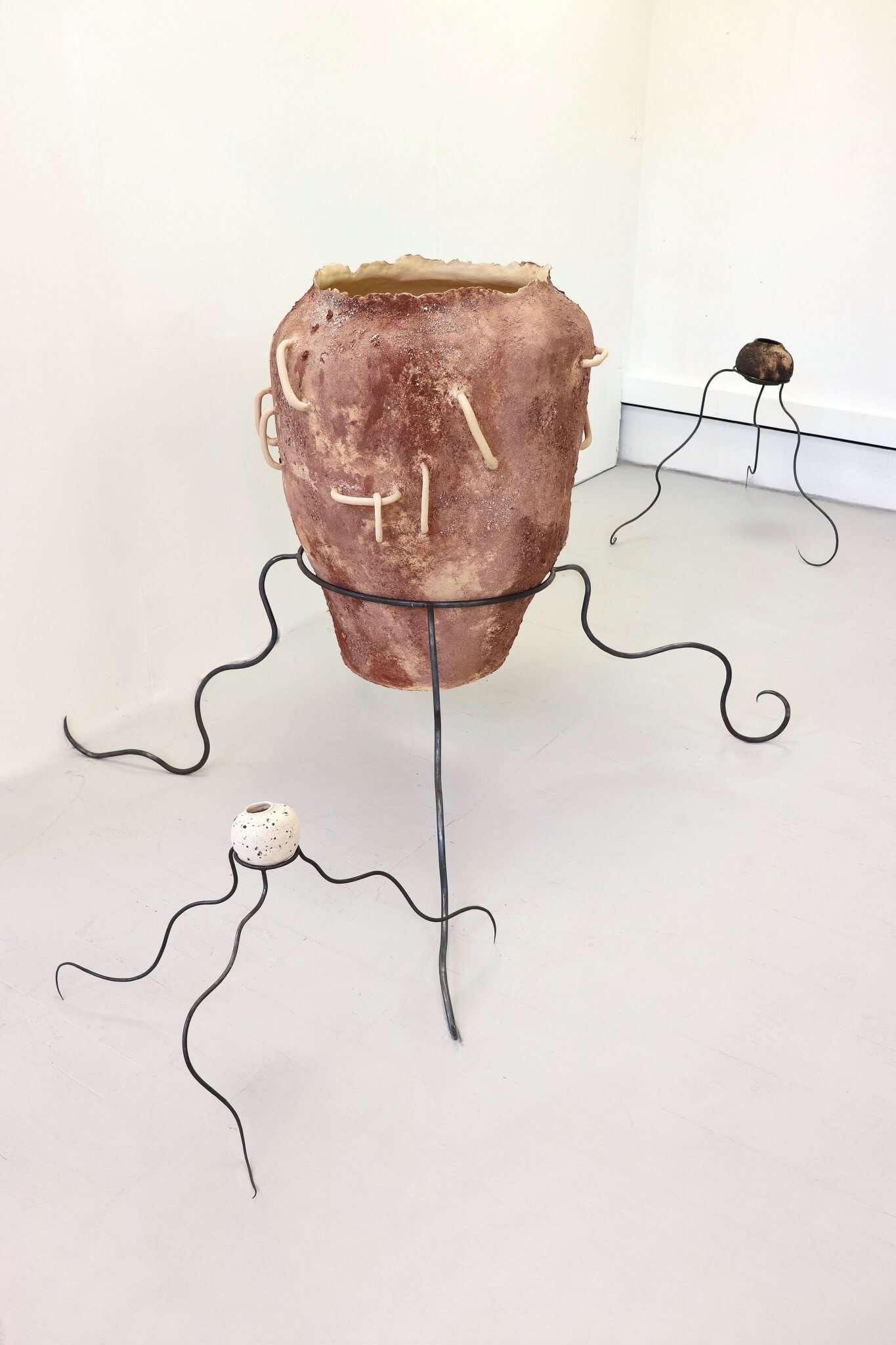 Two small ceramic pots with steel bendy legs lay on each side of a large ceramic pot with longer steel legs.