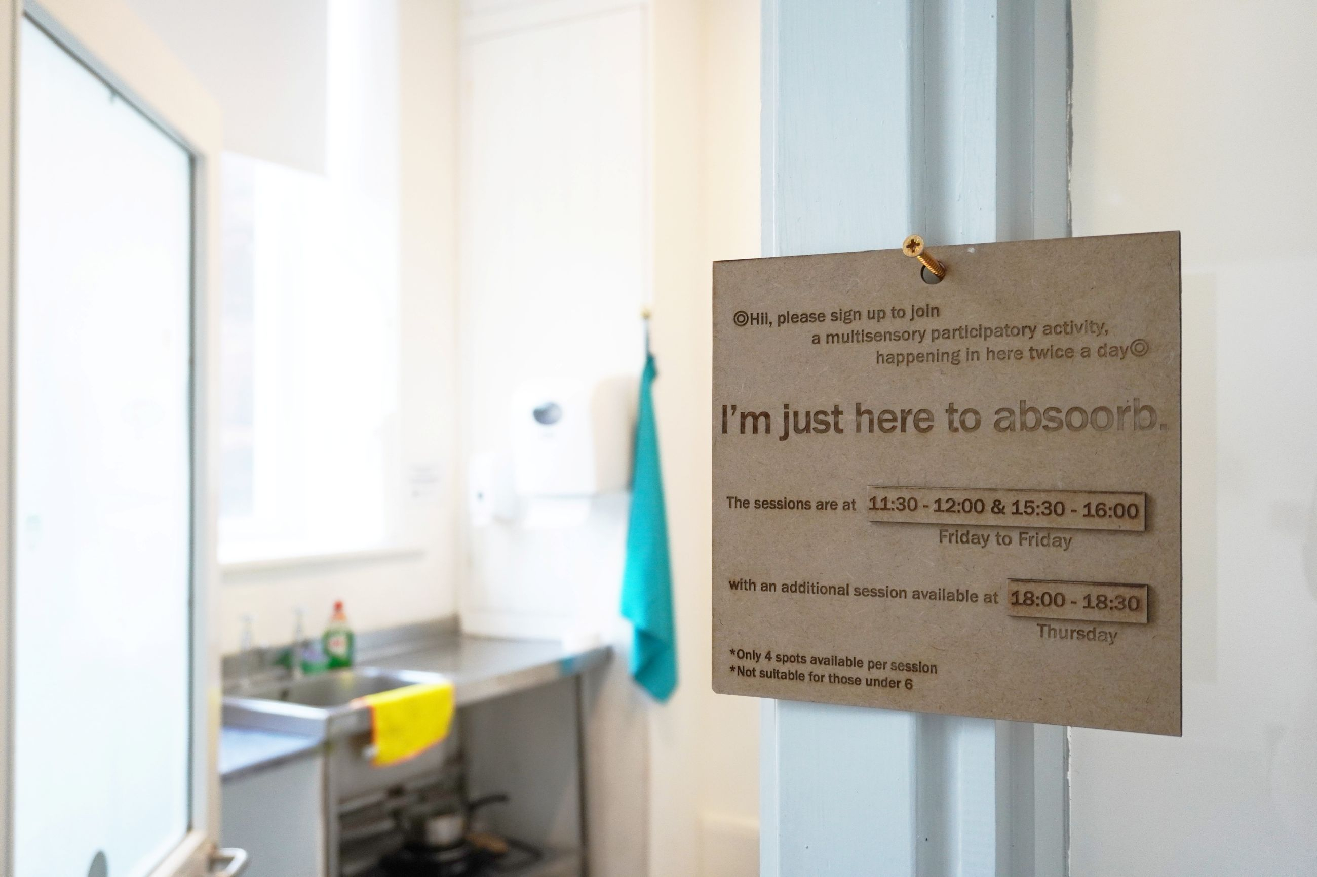 Close-up installation view of 'I'm just here to absooorb.'. A MDF information panel at the entrance of the sink space where the work happened