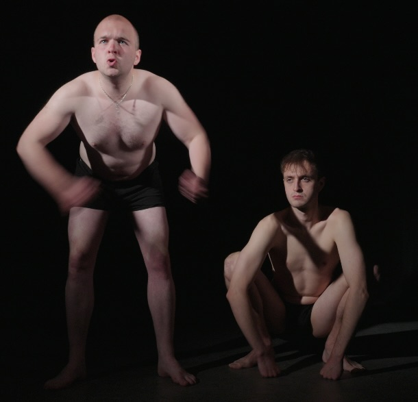 Two men pretending to be monkeys. One beats his chest and one squats with his arms draped over his legs