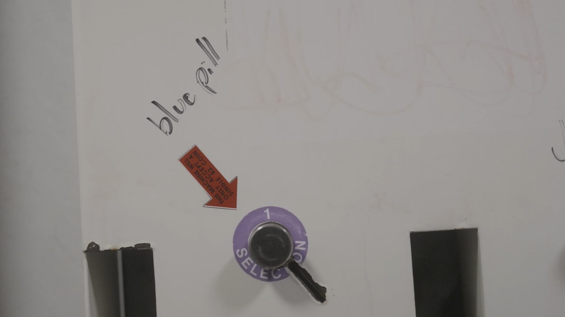 close up of a bathroom vending machine with the words blue pill graffitied