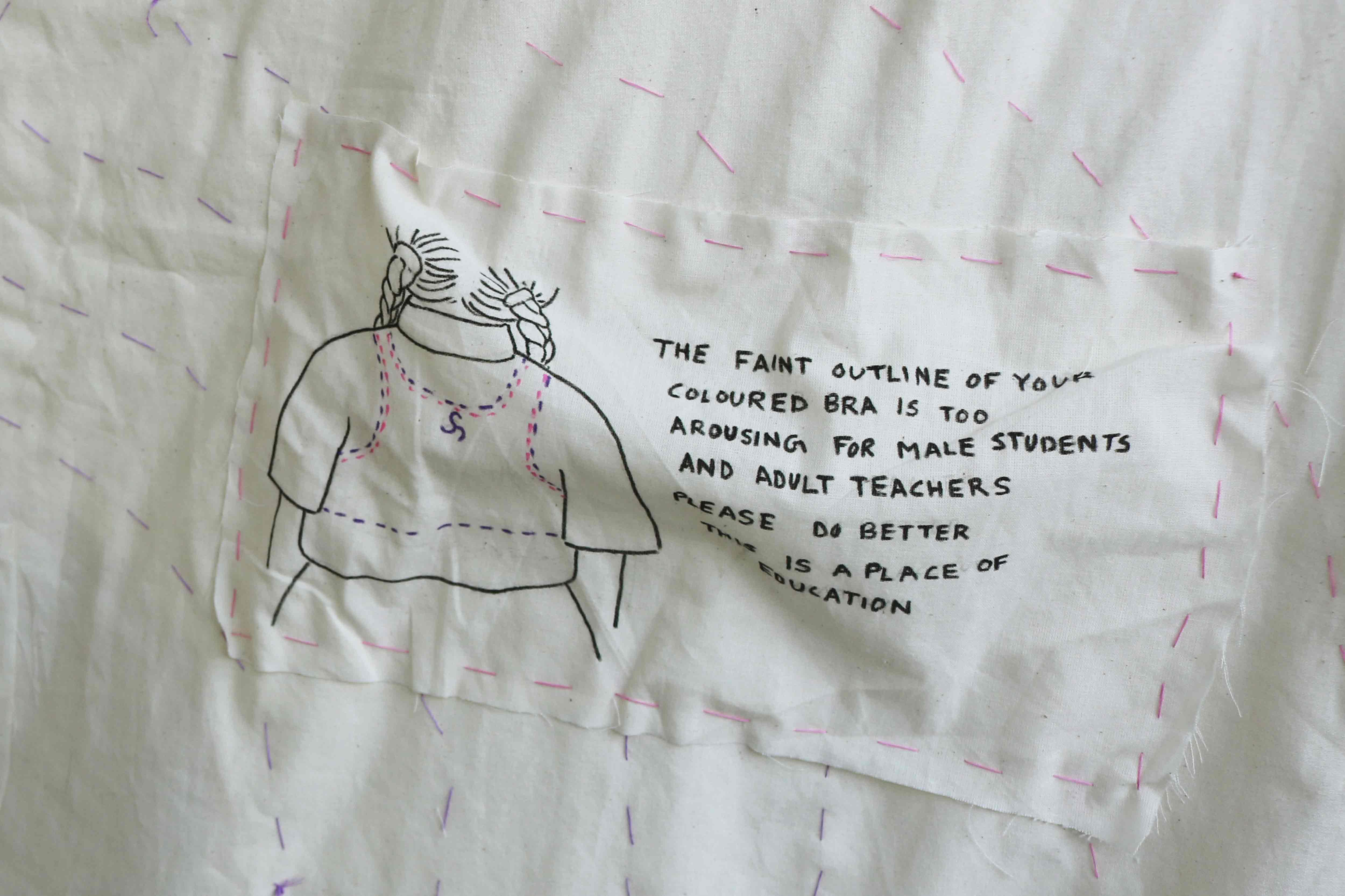 Close up image of Quilt, "Is it Dysphoria or is it Shame" - A patch sewed on to the quilt showing an illustration of a braided young person in school uniform shown from the back with the text "The faint outline of your bra is too distracting for the male students and teachers please do better this is a place of education"
