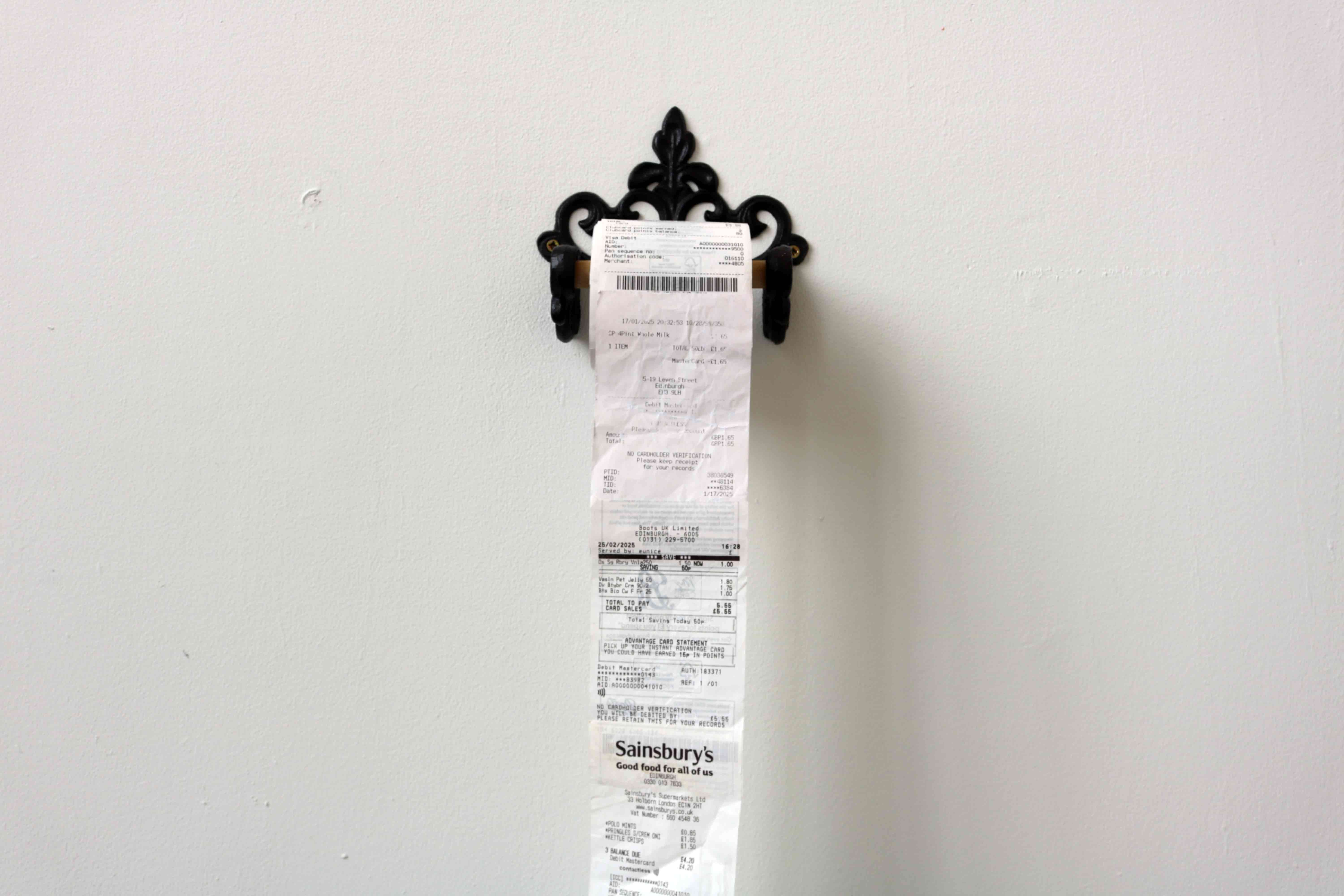 Close up image of artwork 'Roll of Receipts' from the front, displayed on toilet paper holder mounted to wall