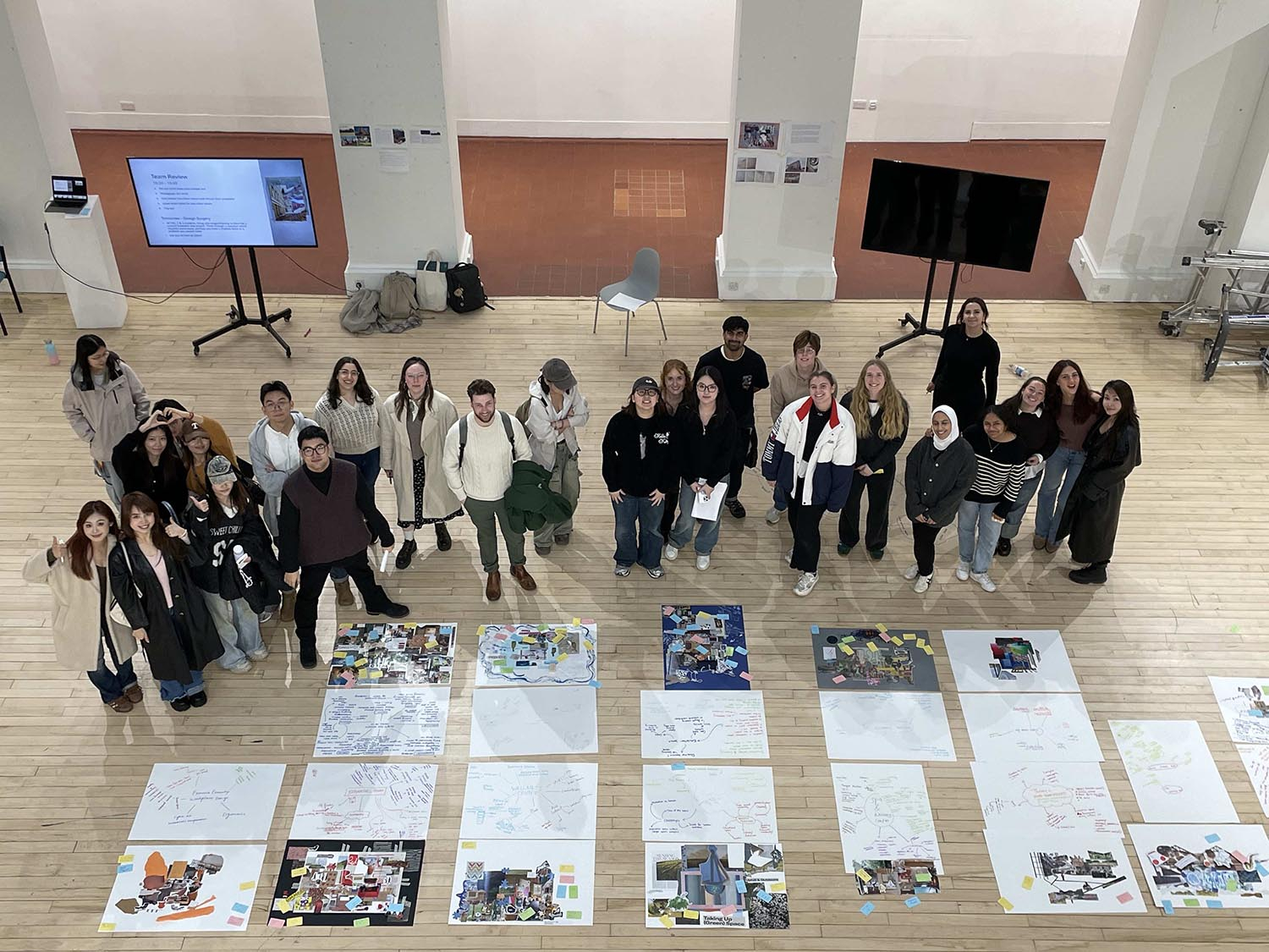 A photo of a group of students taken from the balcony of ECA's Sculpture Court balcony. The students are smiling and looking up at the camera.